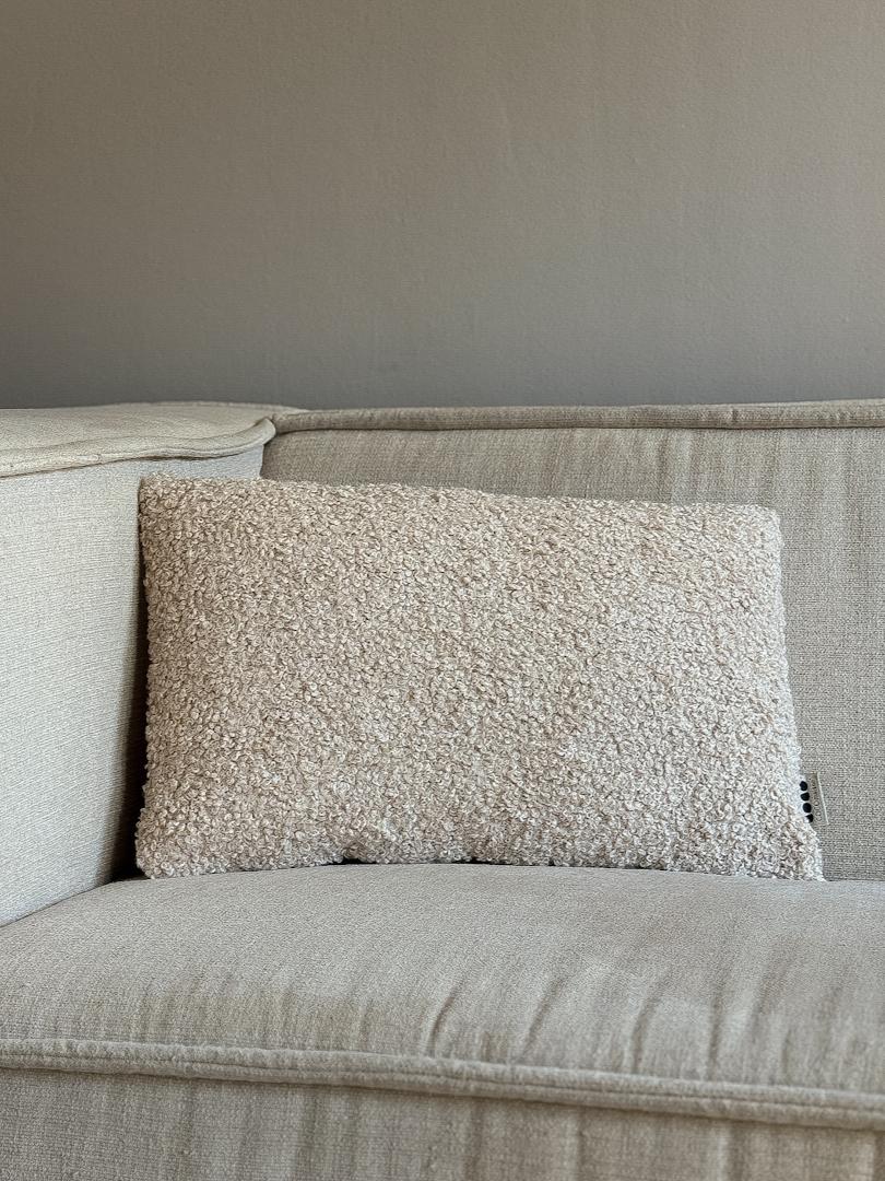 Beige rechthoekig sierkussen met een zachte boucléstof aan de voorkant en een glanzende achterkant.